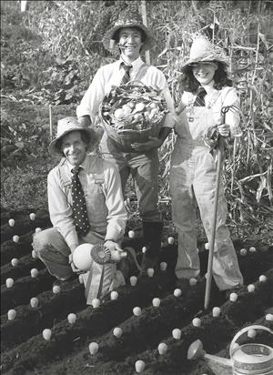 Three white people in straw hats kneel and stand over rows of lightbulbs planted in the dirt like crops